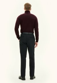 Bordeaux coltrui en zwarte slim fit broek, met een gladde textuur en een eenvoudig ontwerp, gecombineerd met zwarte schoenen.