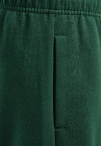 Mörkgröna sweatpants av mjukt, texturerat tyg. Har ett elastiskt midjeband och sidoficka, med en smalare ben design.