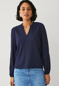 Blusa a maniche lunghe blu navy con scollatura a V e spalle arricciate. Tessuto leggero e testurizzato, vestibilità morbida e polsini elasticizzati.