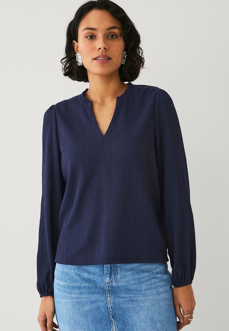 Blusa a maniche lunghe blu navy con scollatura a V e spalle arricciate. Tessuto leggero e testurizzato, vestibilità morbida e polsini elasticizzati.