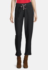 Svarta randiga byxor med dragsnöre i midjan, med sidofickor och manchetter vid fållen, bärs tillsammans med bruna mocka ankelskor.