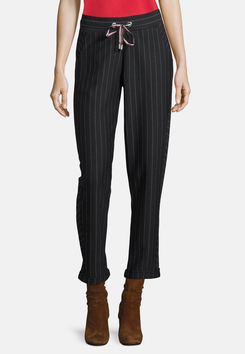 Svarta randiga byxor med dragsnöre i midjan, med sidofickor och manchetter vid fållen, bärs tillsammans med bruna mocka ankelskor.