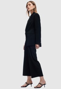 Czarna marynarka o dopasowanym kroju, w zestawie z szerokimi spodniami w tym samym kolorze. Czarne sandały na obcasie i minimalne akcenty metalowe na marynarce.
