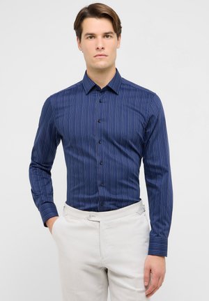 Camicia blu navy con pinstripes verticali, colletto button-down, maniche lunghe e design aderente. Realizzata in tessuto liscio.