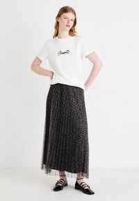 Weißes T-Shirt mit dem Wort "Dream" in schwarzer Kursivschrift, kombiniert mit einem langen, plissierten schwarzen Rock im Leopardenmuster und schwarzen Ballerinas.
