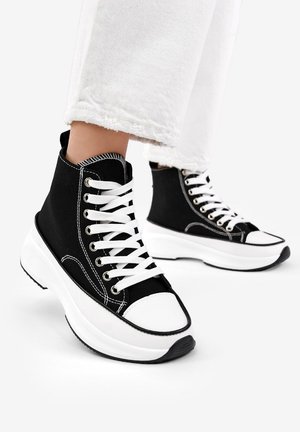 Schwarze High-Top-Sneaker aus Canvas mit weißer Gummisohle. Zu den Merkmalen gehören weiße Schnürsenkel, Metall-Ösen und eine kontrastierende Zehenkappe.