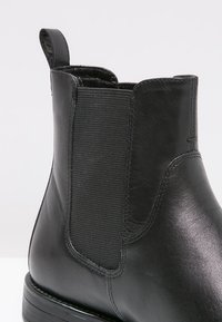 Botte Chelsea en cuir noir avec panneau latéral élastique et languette de tirage, montrant une texture lisse et un détail couturé.