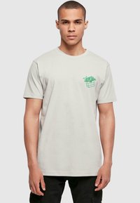 T-shirt in cotone grigio chiaro con maniche corte e collo rotondo, caratterizzato da una grafica verde di patatine in un contenitore sul lato sinistro del petto.