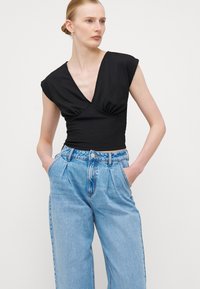 Μαύρο κοντομάνικο τοπ με βαθύ V λαιμόκοψη και ραμμένο μπροστά, συνδυασμένο με ψηλόμεσα ανοιχτό μπλε τζιν που έχουν πιετάκια και κλείσιμο με κουμπί.