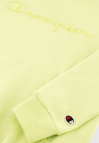 Sudadera verde claro de mezcla de algodón, con un logo bordado de "Champion" y un pequeño logo redondo en el puño.