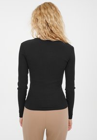 Czarna, długosleeve ribbed bluzka o dopasowanym kroju, z okrągłym dekoltem i gładką teksturą, połączona z beżowymi spodniami o wysokim stanie.