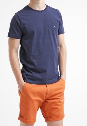 Granatowy bawełniany t-shirt z krótkimi rękawami i okrągłym dekoltem, w połączeniu z pomarańczowymi szortami z podwiniętym brzegiem i bocznymi kieszeniami.