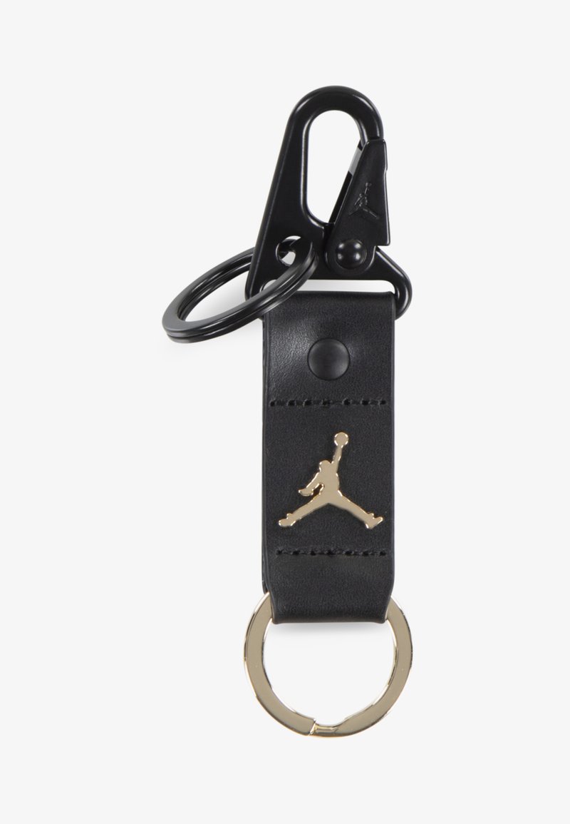 Chaveiro de couro preto com o logo Jumpman dourado, apresentando um anel dourado e um clip preto para fixação. Textura suave com um detalhe de costura discreto.