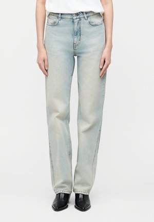 Person iført lyseblå straight-leg jeans med høj talje, kombineret med sorte spidse støvler og en hvid top, der er stukket ned.
