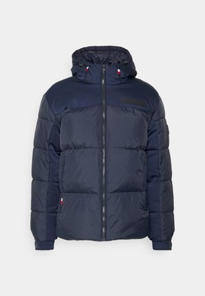 Chaqueta de abrigo acolchada azul marino con capucha, diseño acolchado, cremallera frontal y un parche del logo negro en el pecho. Presenta puños elásticos y bolsillos.