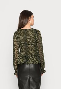 Blusa transparente de estampado de leopardo verde com mangas longas e bainha peplum, combinada com uma saia lápis de couro preta.