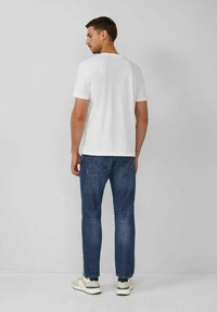 Camiseta blanca de manga corta, corte casual, combinada con jeans de denim azul. Los jeans cuentan con bolsillos traseros y un diseño de pierna recta. Zapatillas blancas completan el look.