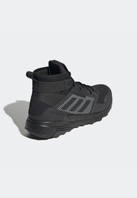 Černé turistické boty s běhounem z textilie a syntetického materiálu, vysokou podporou kotníku, texturovanou gripovou podrážkou a reflexními akcenty po stranách.