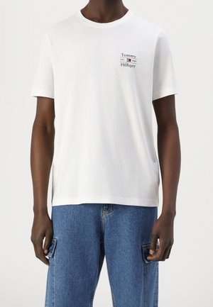 T-shirt en coton blanc à manches courtes, col rond, avec un logo imprimé sur le côté gauche de la poitrine. Associé à un short en jean bleu clair.