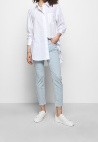White button-up shirt with long sleeves and single chest pocket, paired with light blue striped trousers and white sneakers.