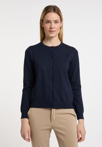 Cardigan blu navy, maniche lunghe, scollatura rotonda, chiusura frontale con bottoni, orlo a coste, texture morbida, abbinato a pantaloni beige.