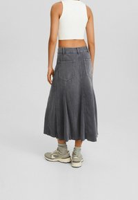 Falda de mezclilla gris con un diseño acampanado, que presenta bolsillos traseros y una longitud a mitad de pantorrilla. Combinada con zapatillas de color claro y calcetines.
