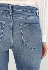Jeans de mezclilla ajustados en azul claro con una textura suave, que cuentan con dos bolsillos traseros y una cintura de altura media con detalles de costura.