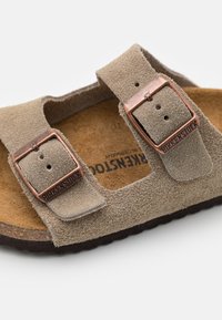 Καφέ σουέτ σανδάλι με δύο ρυθμιζόμενες λουρίδες, με χαλκολίθινα κούμπωμα και φελλώδη σόλα. Υφασμάτινη επιφάνεια, ανοιχτή �μπροστά σχεδίαση.