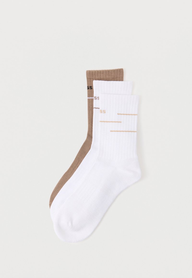 Deux paires de chaussettes côtelées montantes, une blanche avec des rayures beiges et une marron avec du texte noir, posées à plat sur un fond blanc.