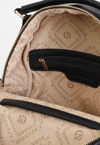 Svart läderryggsäckens insida har en beige foder med upprepat "CAFÉ NOIR"-logotyp. Inkluderar en dragkedjeficka med guldbeslag.