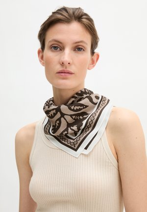 Vrouw met kort haar, een beige geribbelde tanktop en een bruin-witte zijden sjaal met patroon om haar nek.