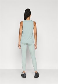 Svetlozelený atletický tank top a legíny z hladkej elastickej látky. Oblečenie je doplnené čiernymi atletickými topánkami.