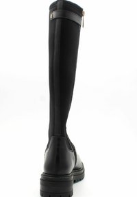 Botas negras hasta la rodilla con una base de cuero suave, un eje de tela elástica y un detalle de cremallera en la parte posterior. Suela de goma gruesa.