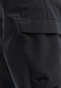 Zwarte broek met een platte tailleband, textuurstof en een zijzak. De stof vertoont een subtiel patroon, waardoor het een strakke uitstraling heeft.