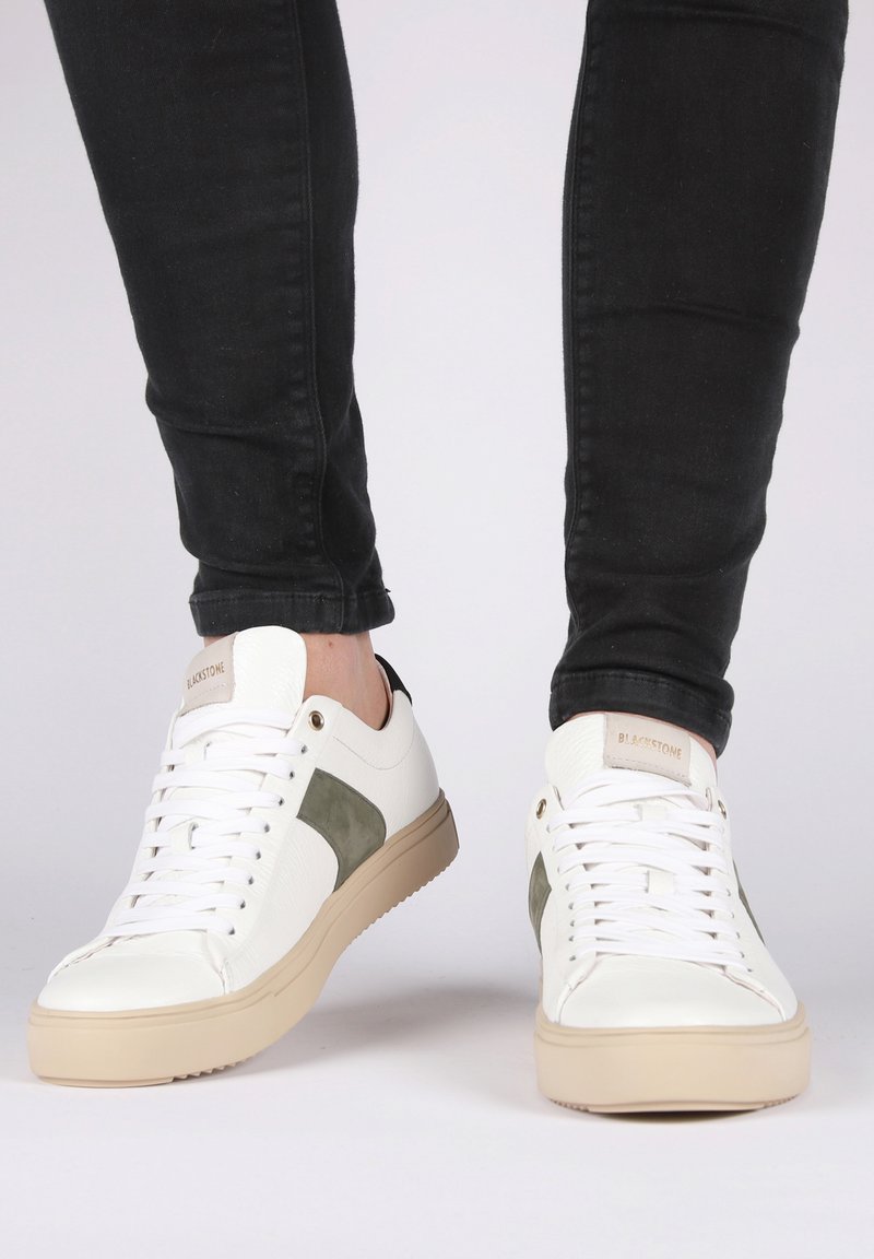 Zapatillas blancas con acabado texturizado, acentos de ante verde oliva y suelas de goma beige. Diseño con cordones y ojales de metal.