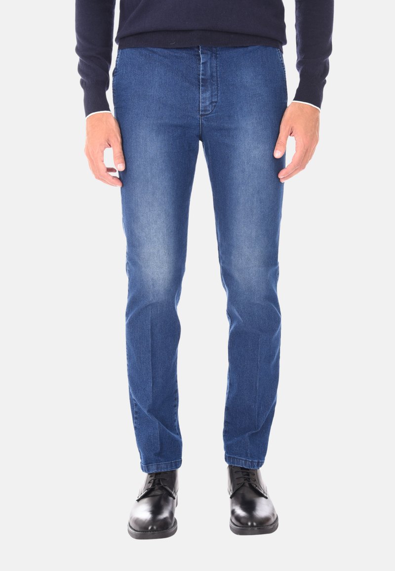 Jeans in denim di blu medio con design slim fit, caratterizzati da uno stile classico a cinque tasche e una superficie liscia. Indossati con scarpe eleganti nere.