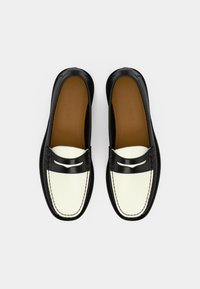 Mocassins de couro em preto e branco com bico redondo, detalhes decorativos em costura e uma superfície lisa e polida, com uma palmilha em tom de caramelo.