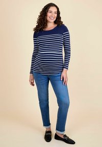 Sinine ja valge triibuline pika varrukaga raseduspael, mis on kombineeritud üleskeeratud äärega siniste teksade ja mustade mokassiinidega; sile tekstuur, juhuslik disain.