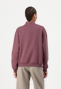 Purple sweatshirt with a high collar, ribbed cuffs, and hem. Made of soft, textured fabric. Paired with light beige pants.