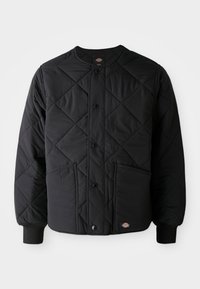 Jachetă neagră matlasată cu butoane tip snap, două buzunare frontale, manșete ribbate și un mic patch cu logo vizibil la marginea din față.