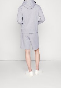 Sudadera con capucha gris combinada con pantalones cortos gris a juego. La tela parece suave con una textura sutil. El modelo lleva zapatillas blancas.