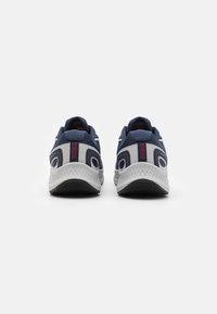 Zapatillas deportivas con una parte superior de malla en azul marino y gris, diseño curvado, cuello acolchado y suela blanca texturizada con detalles en negro.