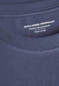 Tamsiai mėlyna medvilninė marškinėlių su riboje apykakle. Etiketėje rašoma "JACK & JONES ORIGINALS," "Pagaminta Bangladeše," ir "Dydis L."