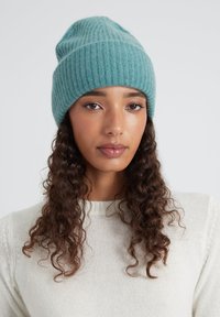 Beanie verde scuro a coste realizzato in morbido materiale di maglia, con un design bicolore, una superficie liscia e una vestibilità aderente sulla testa.