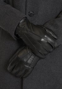 Guanti in pelle nera con dettagli cuciti, indossati sopra un cappotto di lana grigio scuro. I guanti presentano una vestibilità aderente e sezioni delle dita definite.