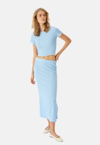 Top corto de color azul claro y falda midi a juego, confeccionados en tejido texturizado. Presenta un patrón acanalado y una abertura lateral en la falda. Diseño casual.