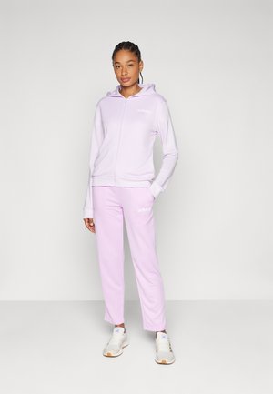 Svetlofialová mikina na zips s prednými vreckami, skombinovaná s namiestnými teplákmi. Obe časti majú bielu vyšívanú ikonu Adidas.