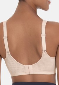 Beige draadloze beha van textuurstof, met brede verstelbare banden en een haak-en-oog sluiting aan de achterkant. Heeft een gladde, naadloze uitstraling.
