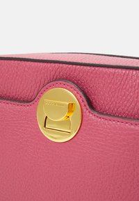 Borsa a mano in pelle rosa con superficie texturizzata, dotata di una chiusura circolare dorata e cuciture a contrasto. Design classico con parte superiore arrotondata.