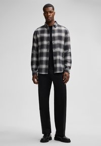 Karierte Flanellshirt in Schwarz und Weiß, mit Knopfleiste, Kragen, kombiniert mit schwarzen Hosen und schwarzen Stiefeln. Glatte Textur, lockere Passform.